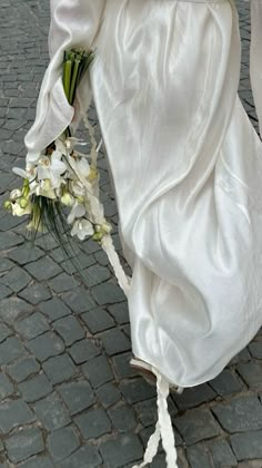 the bride is walking down the street with her bouquet on her hand and wearing a white dress