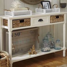 a white console table with baskets on top and two drawers below it, in front of a mirror