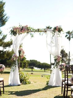 an outdoor wedding setup with white and pink flowers on the arch, chairs in the grass