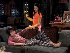 two people sitting on a couch in the living room with one person holding a banana