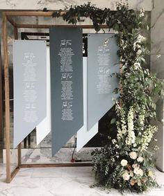 an arrangement of flowers and greenery on display in front of a wall with seating signs