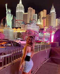 a woman standing in front of the statue of liberty at night with her hand on her hip