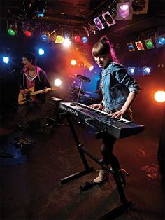 two people playing keyboards in front of colorful lights