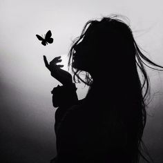 the silhouette of a woman holding a butterfly in her hand