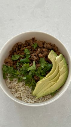 a white bowl filled with rice, meat and avocado on top of it