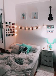 an unmade bed in a small room with string lights on the wall above it