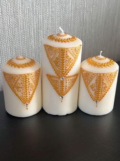 three white candles with gold designs on them