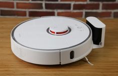 the robotic vacuum is sitting on top of a wooden table next to a brick wall