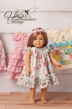 a doll is standing in front of some clothes on a wooden floor and there are two dresses hanging up behind her