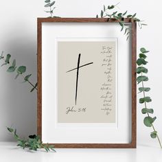 a framed photo with a cross on it next to some green leaves and greenery