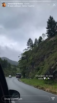 a car driving down a road next to a lush green hillside on a cloudy day