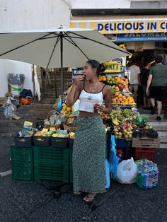 a woman standing in front of a fruit stand with an umbrella on the side walk