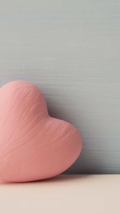 a pink heart shaped object sitting on top of a white table next to a gray wall