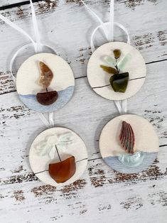 four sea glass ornaments hanging from strings on a white wooden surface with seashells