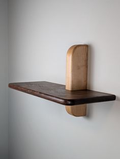 a wooden shelf mounted to the side of a white wall with a wood block on it