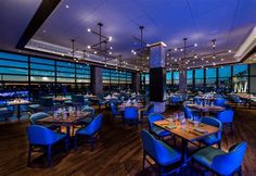 a restaurant with blue chairs and tables in front of large windows overlooking the city at night