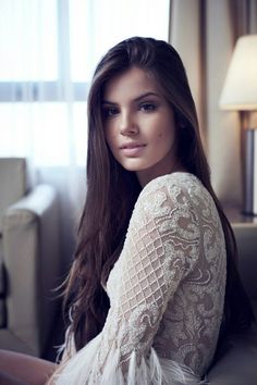 a woman with long hair sitting on a couch in front of a window and looking at the camera