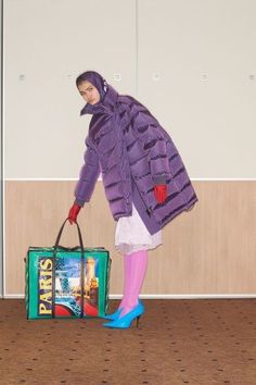 a woman in purple is holding a green bag and wearing pink tights while standing next to a wall