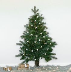 a small christmas tree with white stars on it and presents under the tree, in front of a white wall