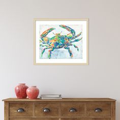 a painting of a colorful crab on a white wall above a dresser with two red vases