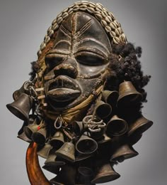 an african mask with bells hanging from it's face and hair in the air