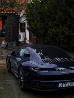 a blue sports car parked in front of a house on a rainy day with no one around