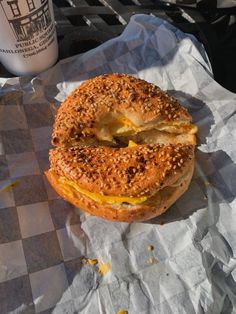 a bagel sandwich sitting on top of a piece of paper next to a cup