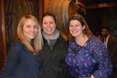 three women standing next to each other in front of wine casks at a winery