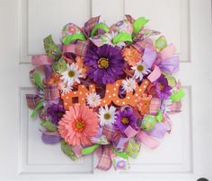 a colorful wreath with the word joy is hanging on a white front door, decorated with flowers and ribbons