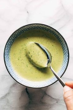 a hand holding a spoon over a bowl of soup