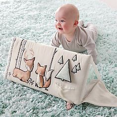 a baby is laying on the floor with a blanket that has pictures of deers and trees