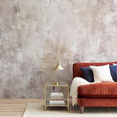 a red couch sitting in front of a wall with a lamp on top of it