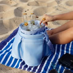 a woman sitting on top of a blue towel next to a bag filled with bottles