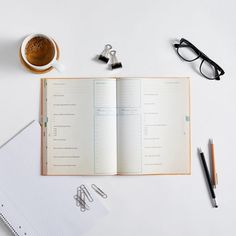 an open notebook on top of a desk next to a cup of coffee and eyeglasses