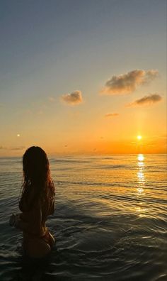 a woman is sitting in the water watching the sun go down over the ocean at sunset