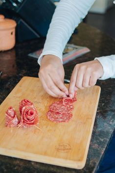 a person cutting up meat on top of a wooden cutting board