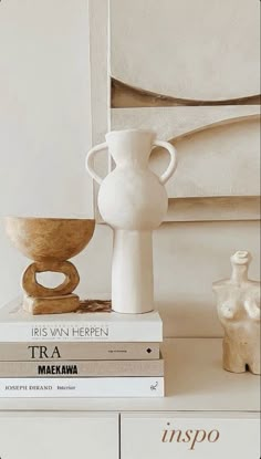 a stack of books sitting on top of a white table next to a vase and bowl