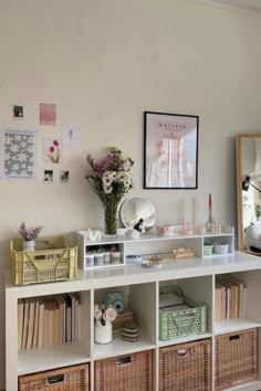 a white shelf filled with lots of books and baskets next to a wall covered in pictures