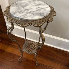 a marble top side table with ornate metal legs and foot rests on a hardwood floor