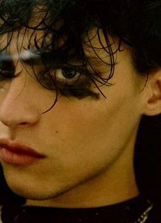 a close up of a person with dark hair and blue eyes wearing a black shirt