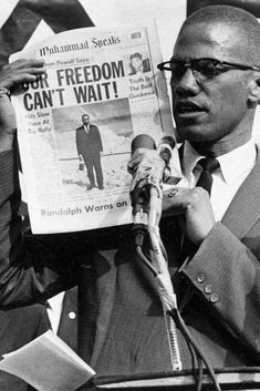 a black and white photo of a man reading a newspaper while holding a microphone in front of him