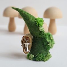 a small green gnome figurine with three mushrooms in the background and a ring on it's finger