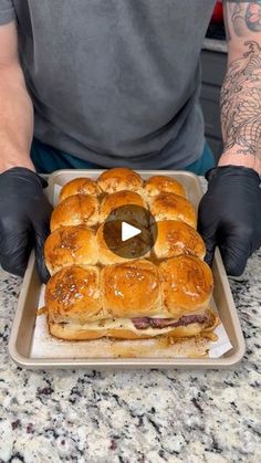 a man with black gloves holding a large sandwich in front of his face on a tray