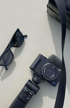 a camera and some sunglasses sitting on a table next to a strap that is attached to a bag