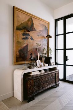 a living room with a painting on the wall next to a table and lamp in front of it