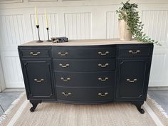 a large black dresser with gold handles and knobs on the top, in front of a white garage door