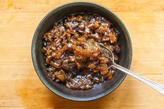 a bowl filled with food sitting on top of a wooden table next to a spoon