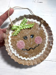 a hand holding a brown paper plate with a face on it and green ribbon around the edge