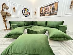 a large green couch sitting on top of a white floor next to a clock and pictures