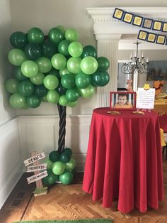 a red table with green balloons on it and a tree in the middle is set up for a party